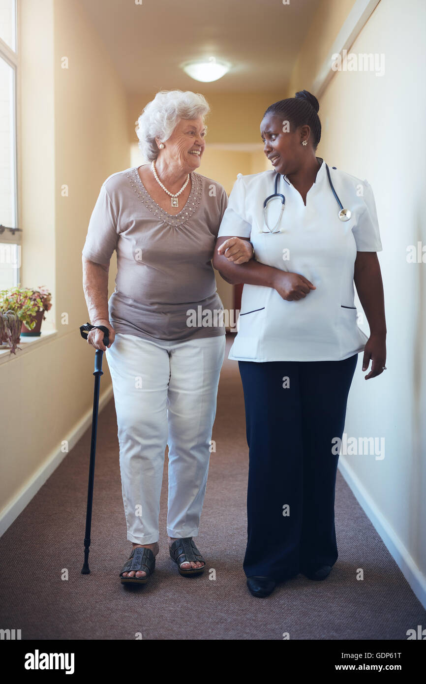 Senior woman with walking stick being helped by female nurse at home. Full length shot of female doctor supporting elderly patie Stock Photo