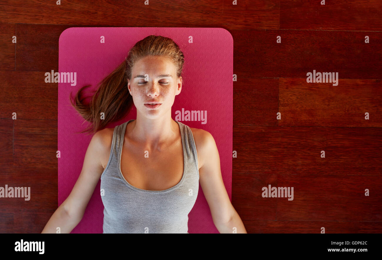 Top view of beautiful young woman lying on exercise mat with her eyes closed at yoga class. Fitness female in corpse pose at gym Stock Photo