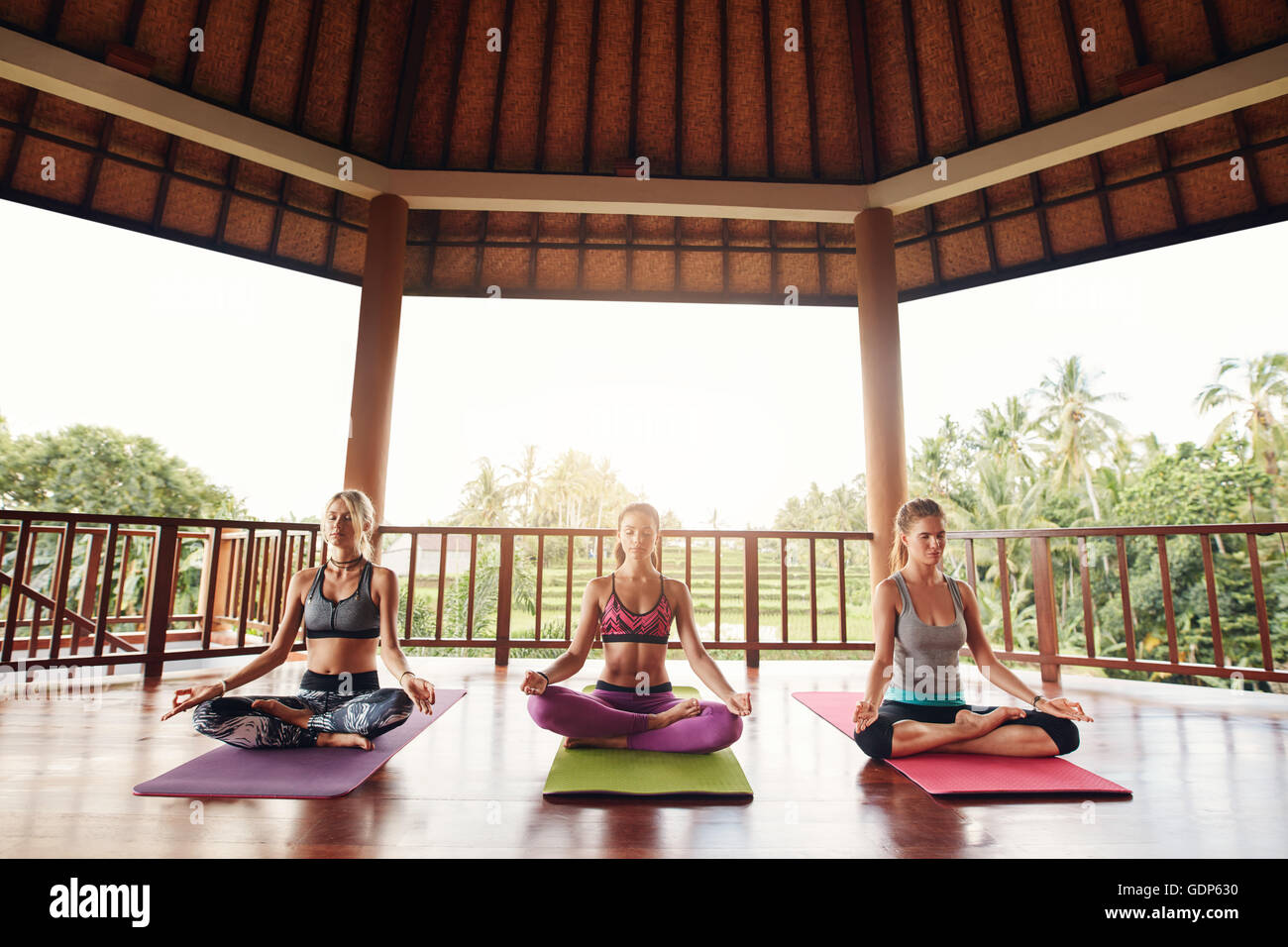 Shot of three young women doing yoga in the class. Fitness people sitting on the exercise mat and relaxing in yoga position. Gro Stock Photo