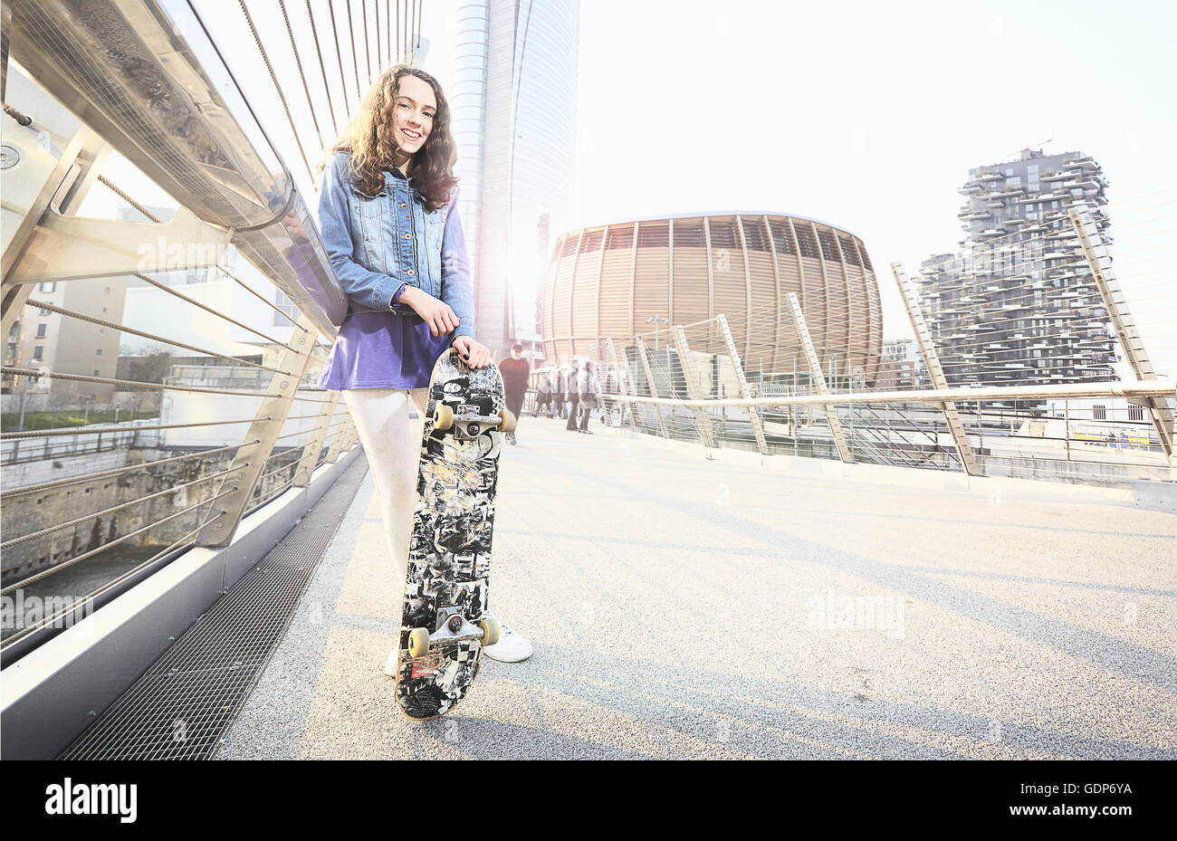 Girl with skateboard leaning against handrail Stock Photo