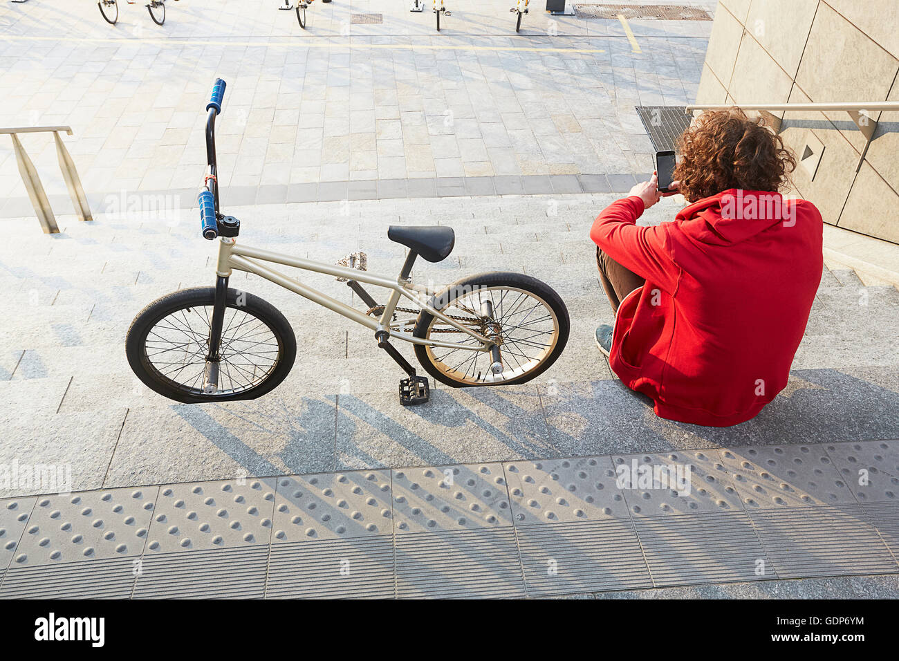 Rear view of man sitting on steps with BMX using smartphone Stock Photo