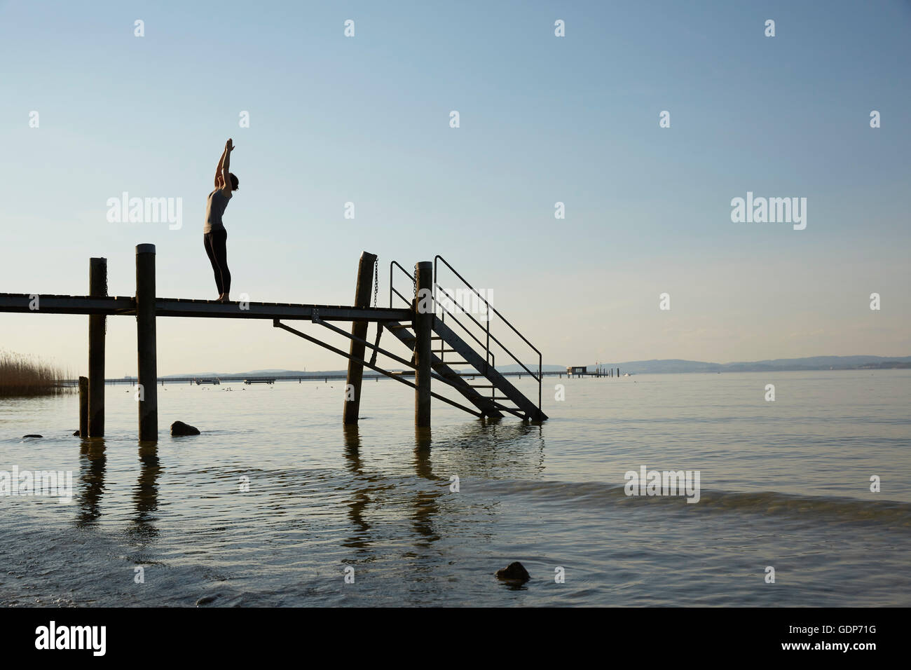 Silhouette of woman on pier arms raised in yoga position Stock Photo