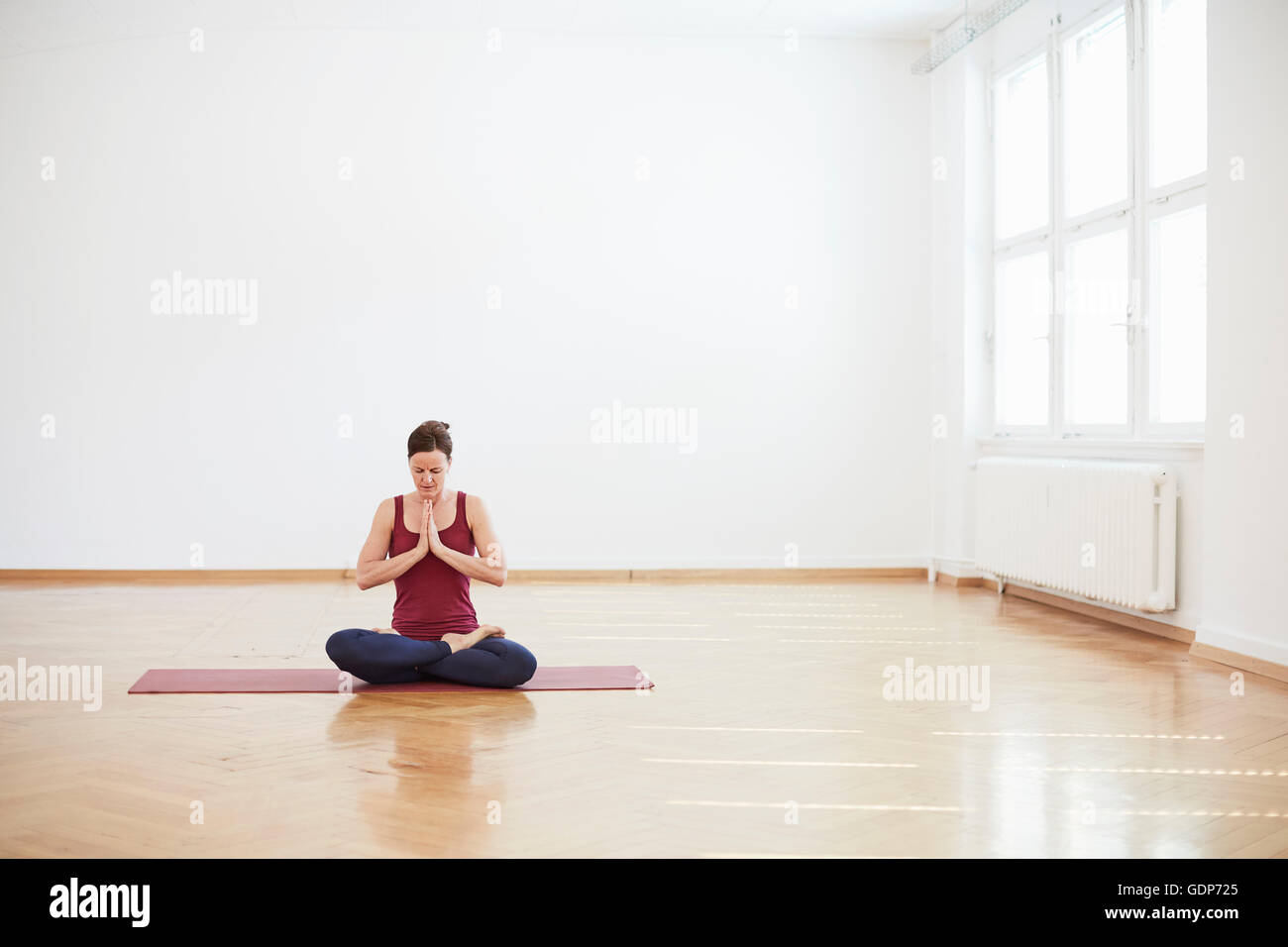 Woman in exercise studio sitting cross legged, hands together meditating Stock Photo