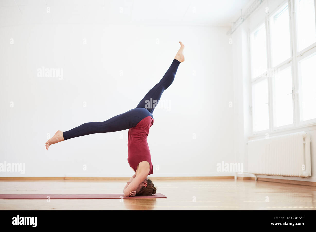 Woman in exercise studio legs apart doing headstand Stock Photo