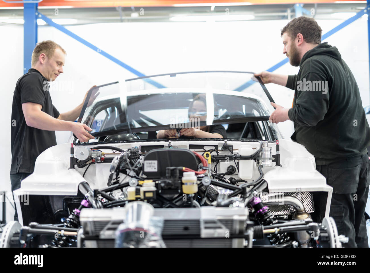 Engineers fitting windscreen to car in racing car factory Stock Photo