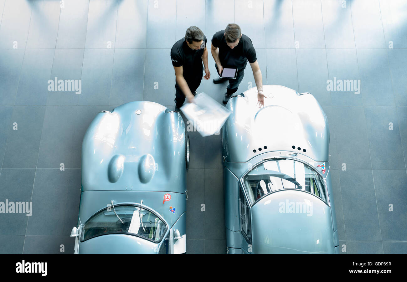 Engineers inspecting classic racing cars in racing car factory, overhead view Stock Photo