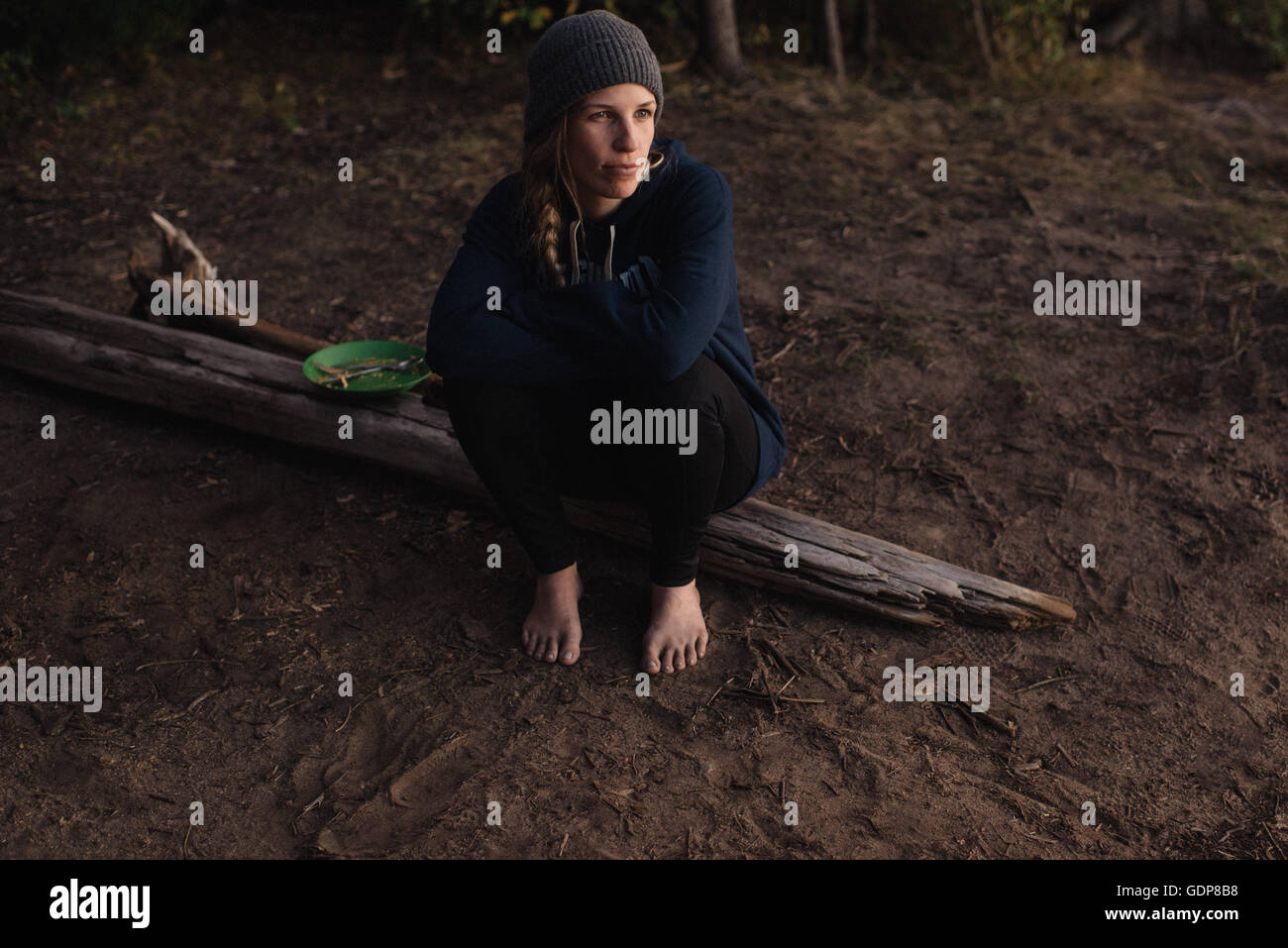 Mid adult woman sitting on wood in forest, looking away Stock Photo