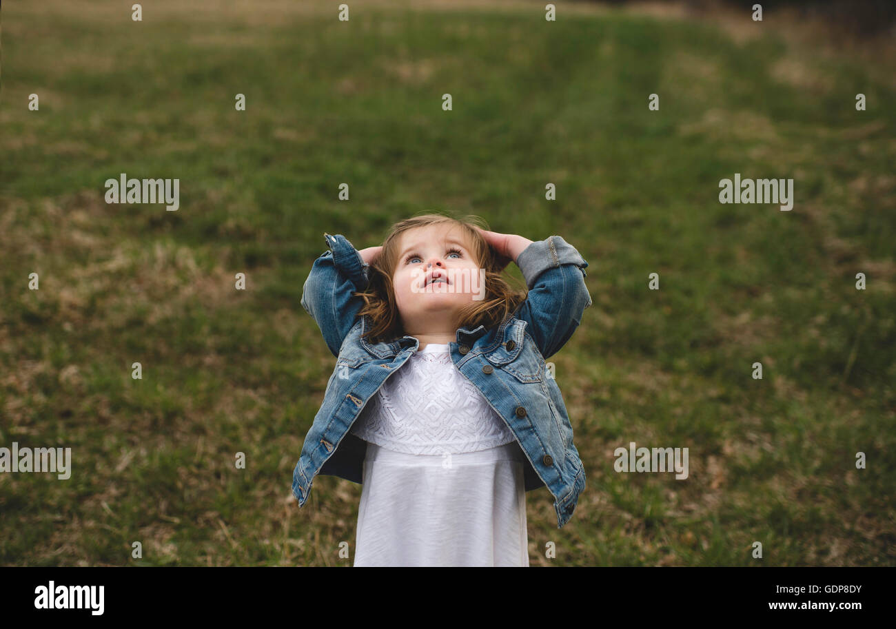 Young girl, in meadow, hands on head looking up into the sky Stock Photo