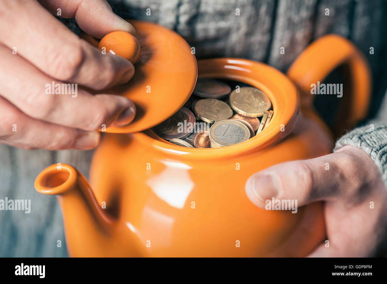 Close up of man's hands holding teapot full of coins Stock Photo