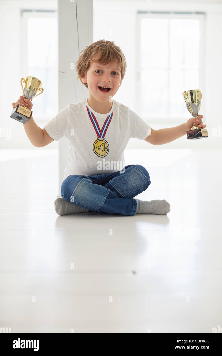 Portrait of boy wearing gold medal holding up trophies Stock Photo