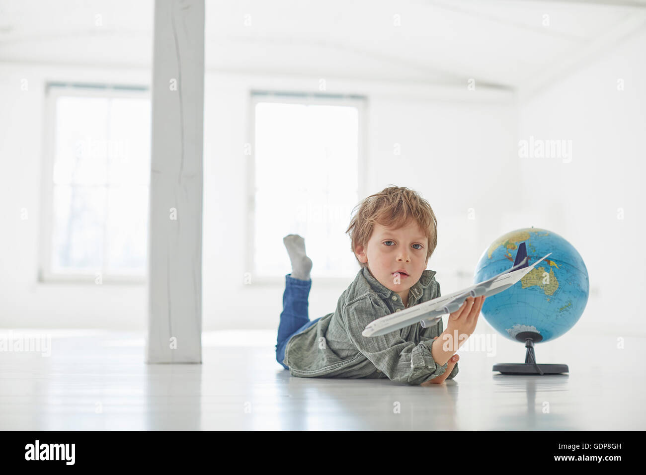 Portrait of boy lying on floor playing with globe and toy airplane Stock Photo