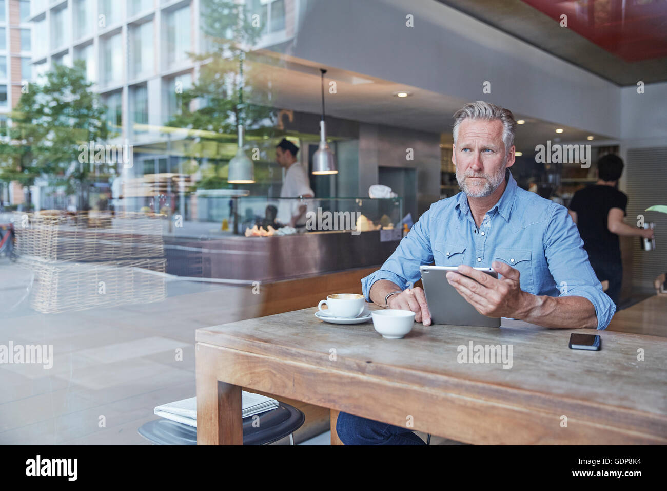 Mature man sitting in cafe, using digital tablet Stock Photo