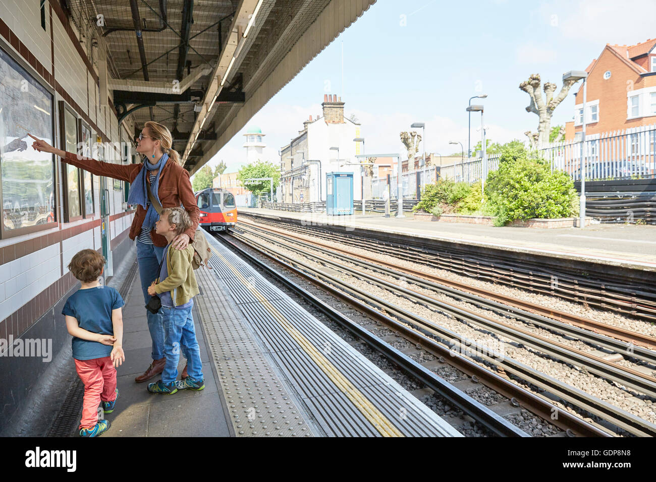 Mother and sons on railway platform looking at wall mounted map Stock Photo