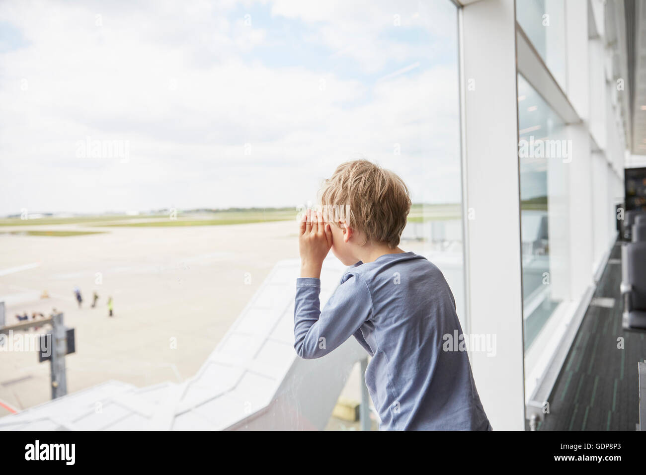 Boy looking out of airport window at runway Stock Photo