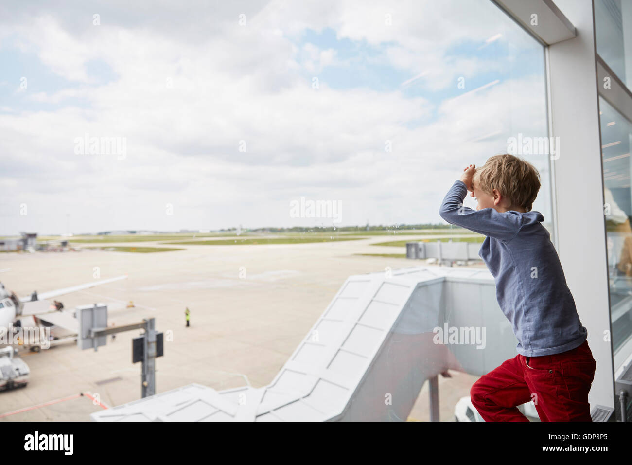 Boy looking out of airport window at runway Stock Photo