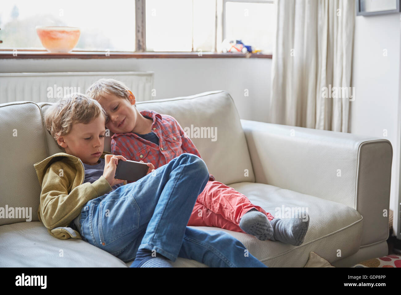 Boys sitting on sofa looking at smartphone Stock Photo