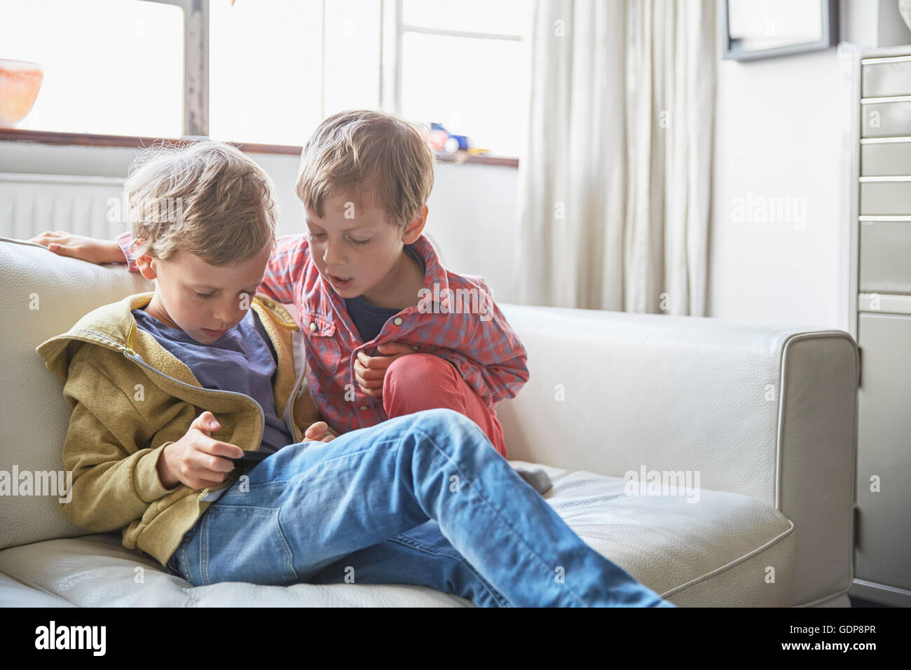 Boys sitting on sofa looking at smartphone Stock Photo