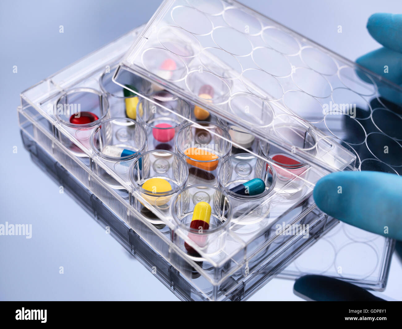 Pharmaceutical research, hand removing lid from variety of medical drugs in a multi well tray for laboratory testing Stock Photo