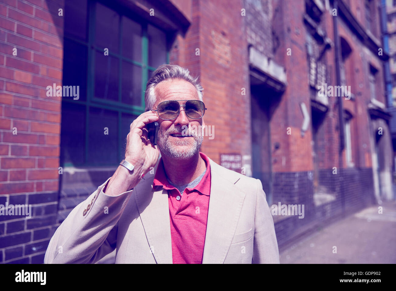 Mature man walking along street, using smartphone Stock Photo