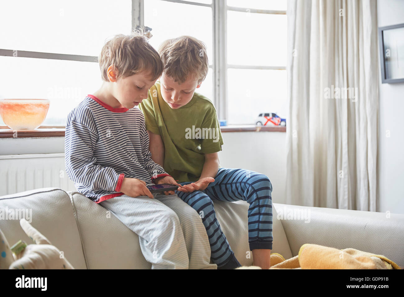 Boys wearing pyjamas sitting on sofa looking at smartphone Stock Photo