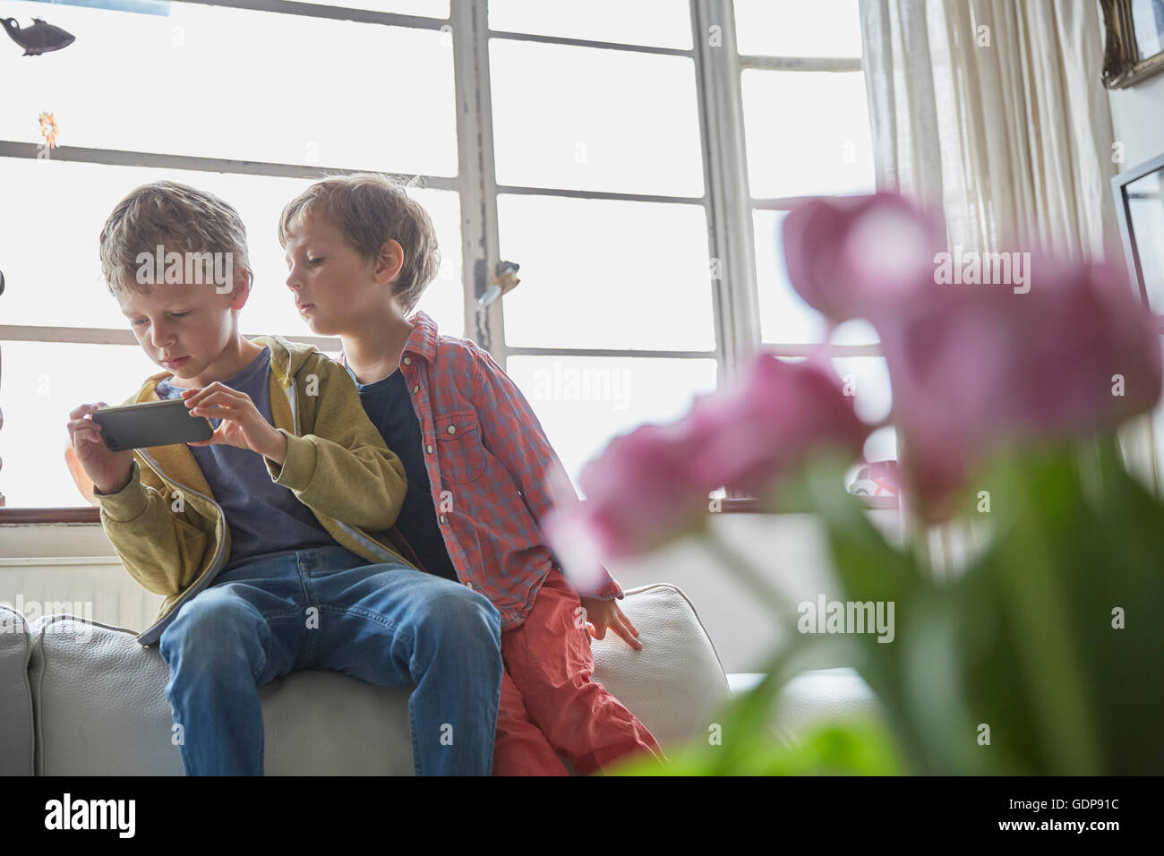 Boy sitting on sofa looking over brother shoulder at smartphone Stock Photo