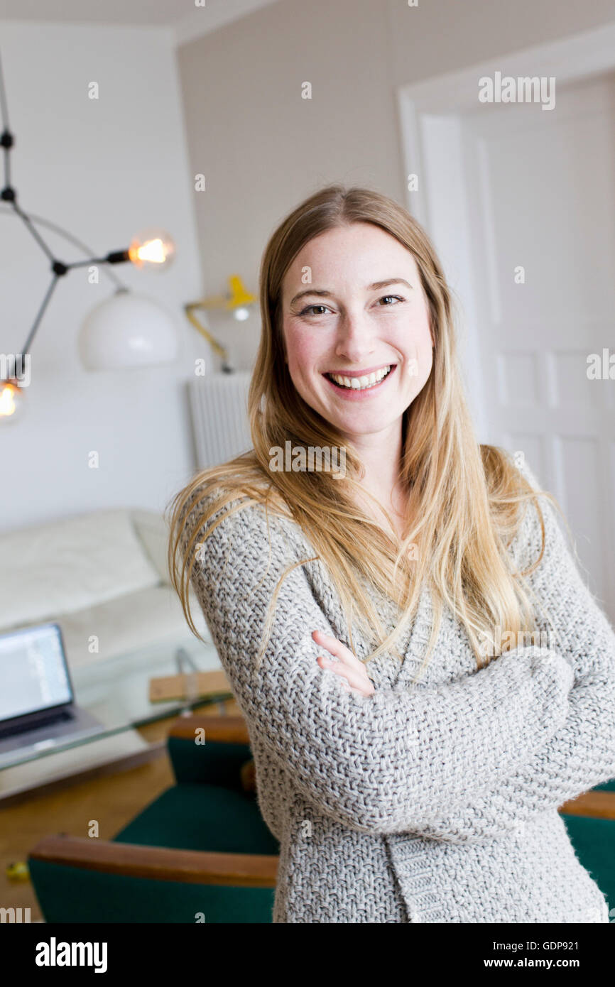 Portrait of happy mid adult woman with arms folded in living room Stock Photo