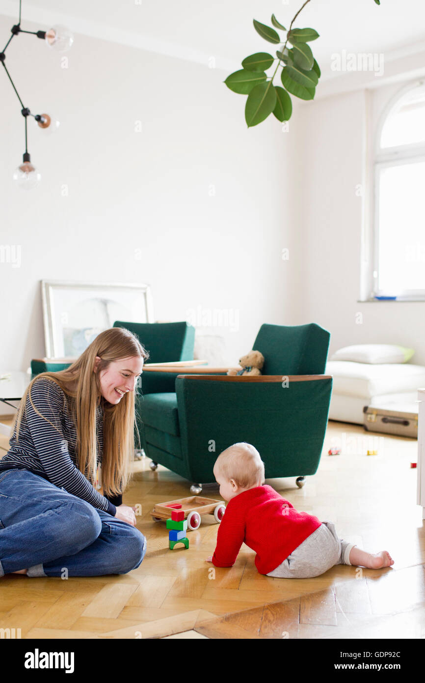 Mid adult woman and baby daughter play with building blocks on living room floor Stock Photo