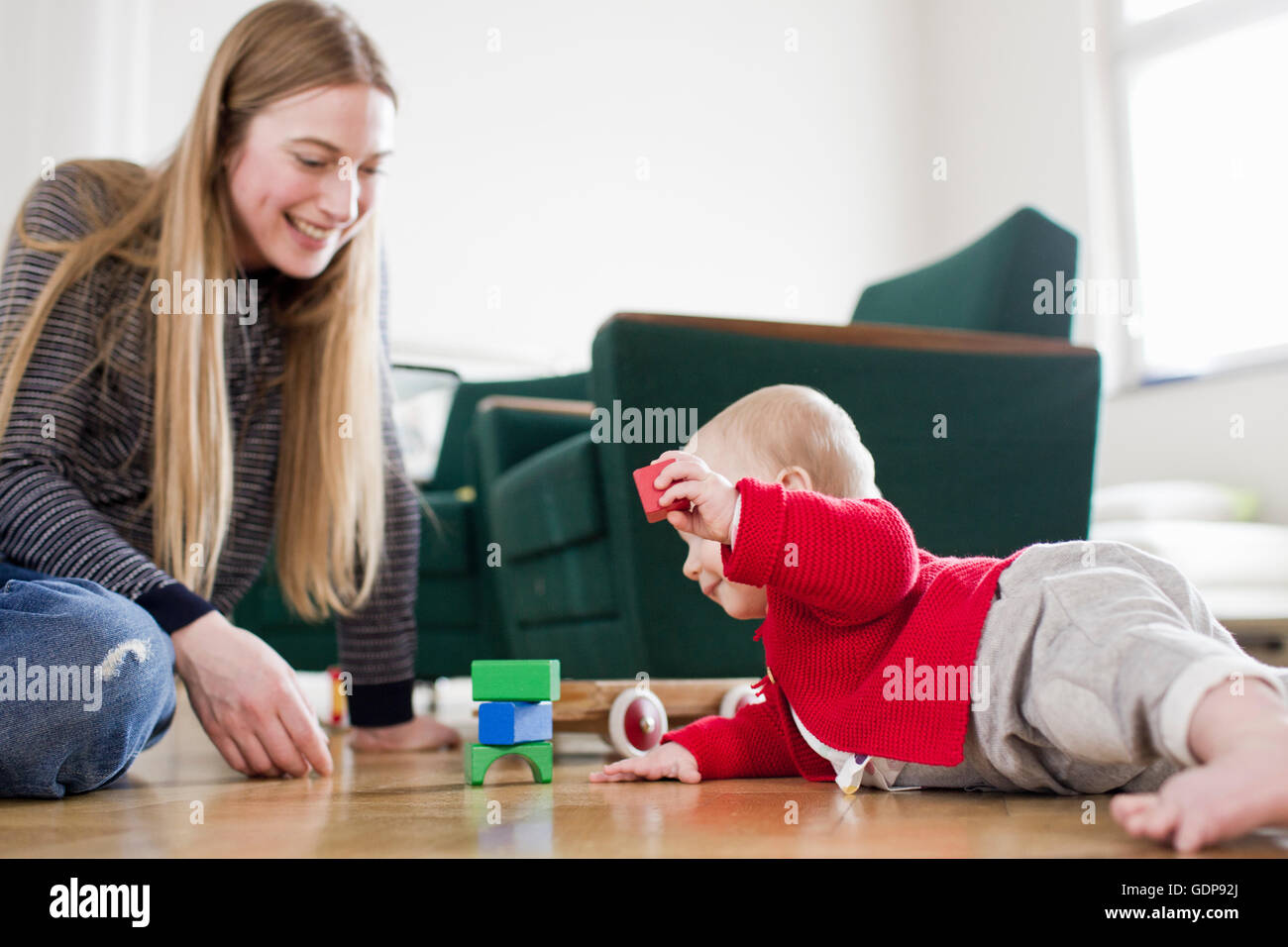 Woman and baby daughter play with building blocks on living room floor Stock Photo