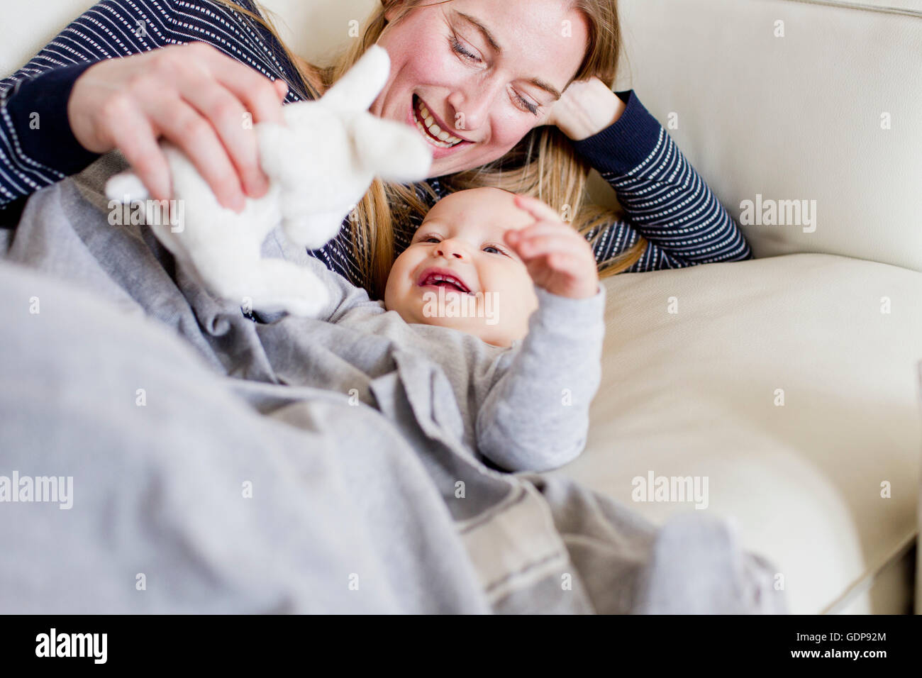 Baby girl and mother playing with toy rabbit on sofa Stock Photo