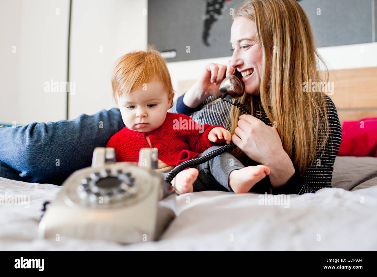 Mid adult woman and baby daughter on bed talking on landline telephone Stock Photo