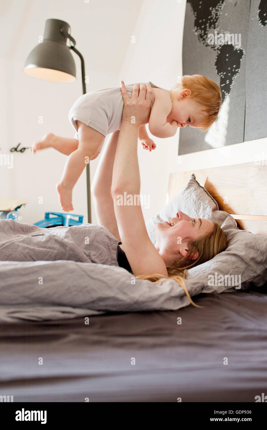 Mid adult woman holding up baby daughter in bed Stock Photo