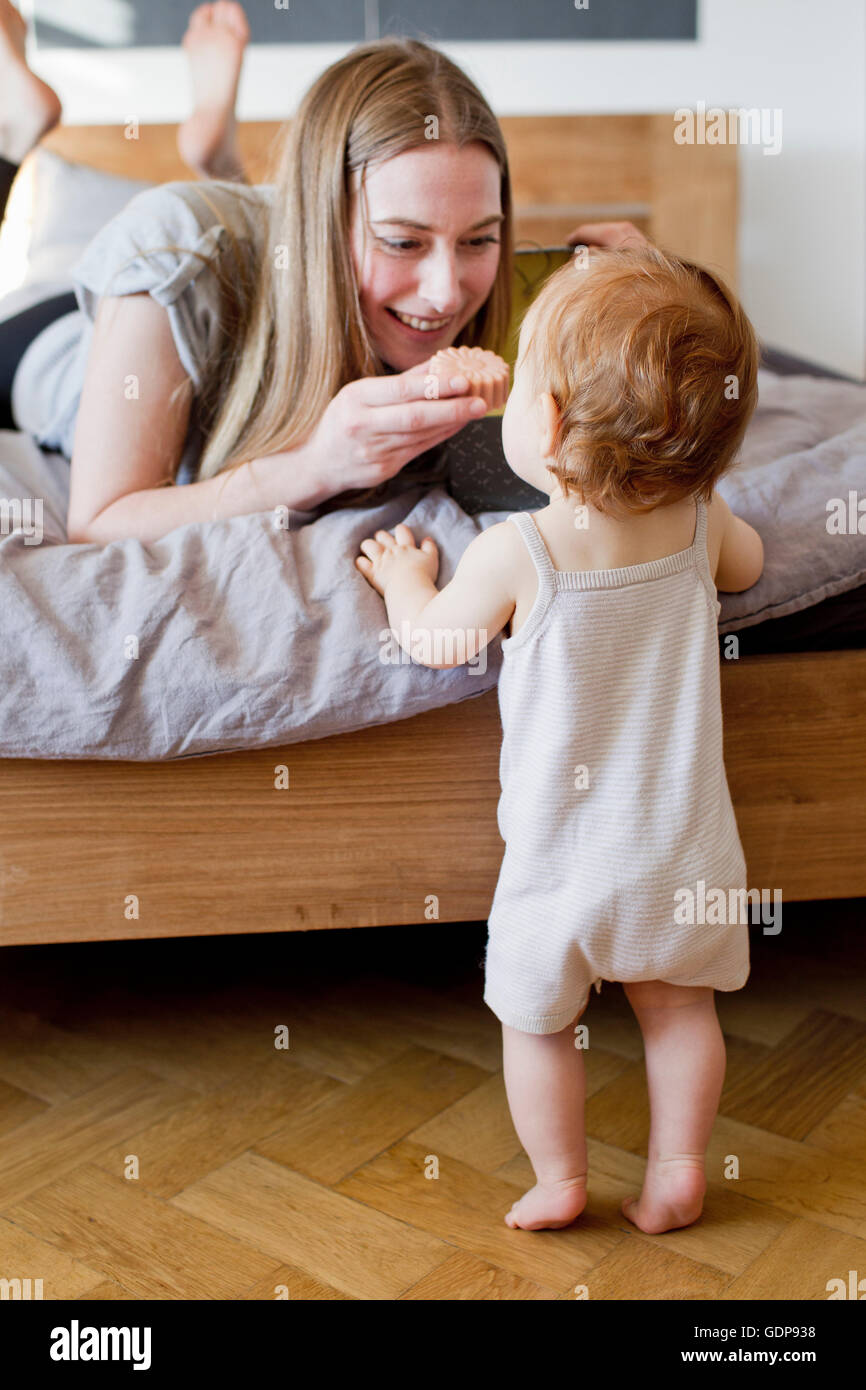 Mid adult woman feeding baby daughter a biscuit from bed Stock Photo
