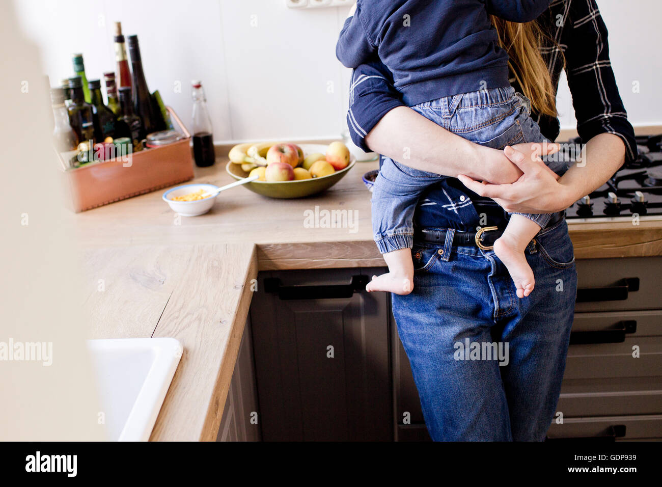 Cropped shot of mid adult woman carrying baby son in kitchen Stock Photo