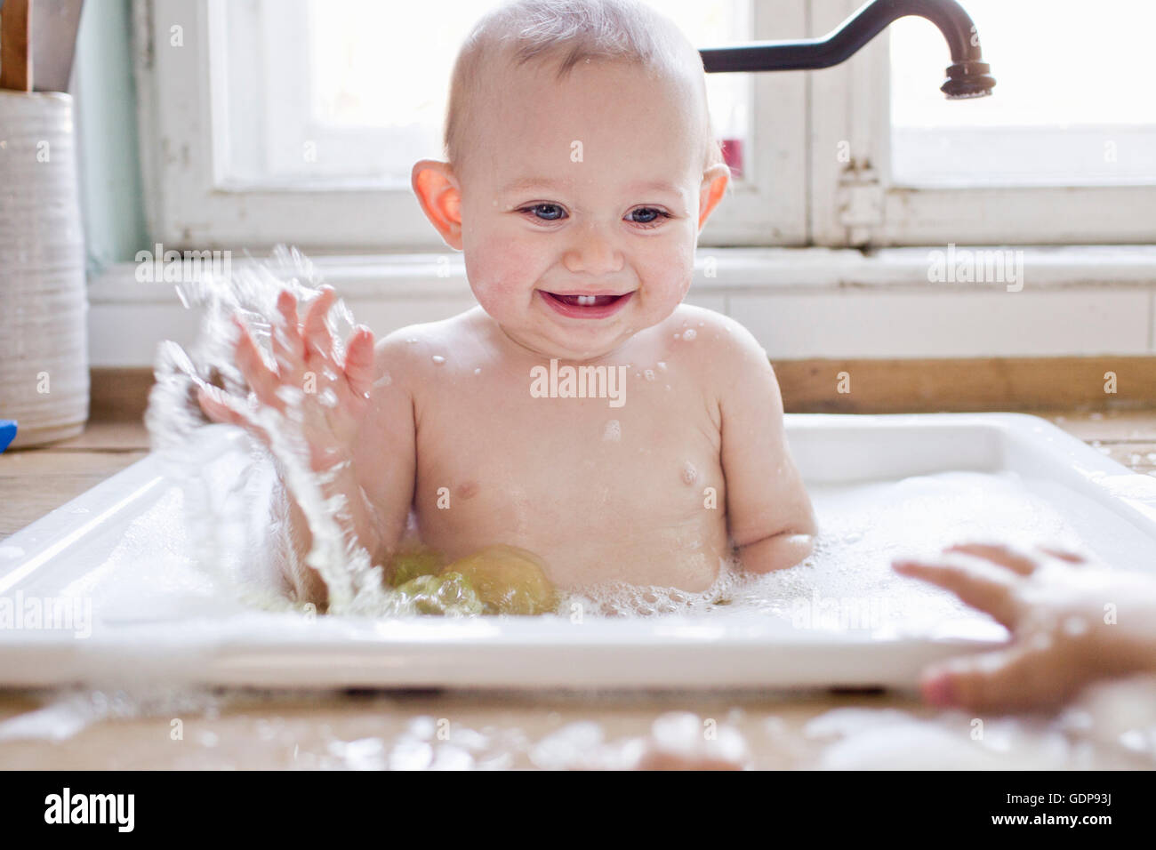 Baby boy splashing whilst bathing in kitchen sink Stock Photo