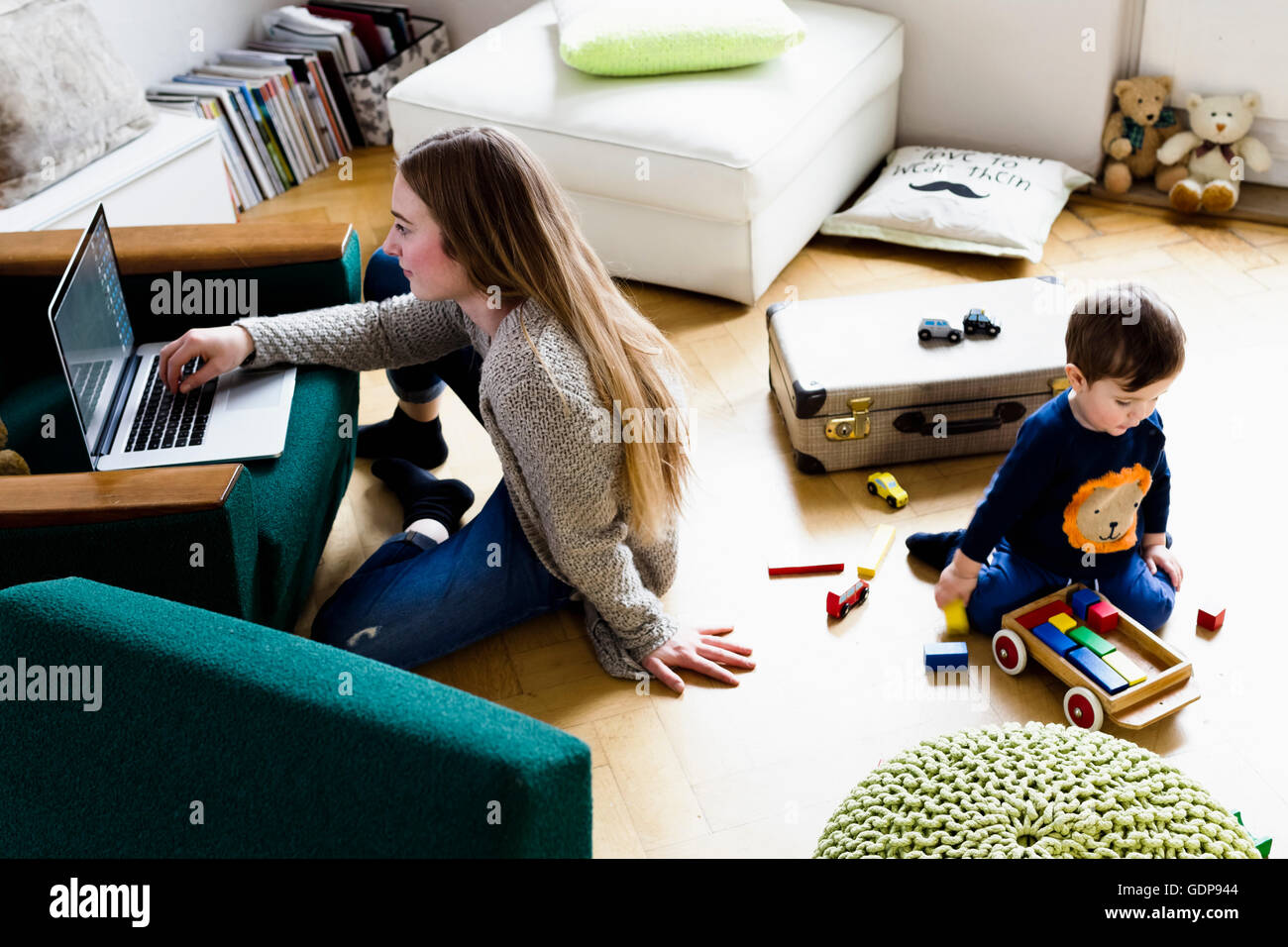Mid adult woman typing on laptop whilst baby son playing on floor Stock Photo
