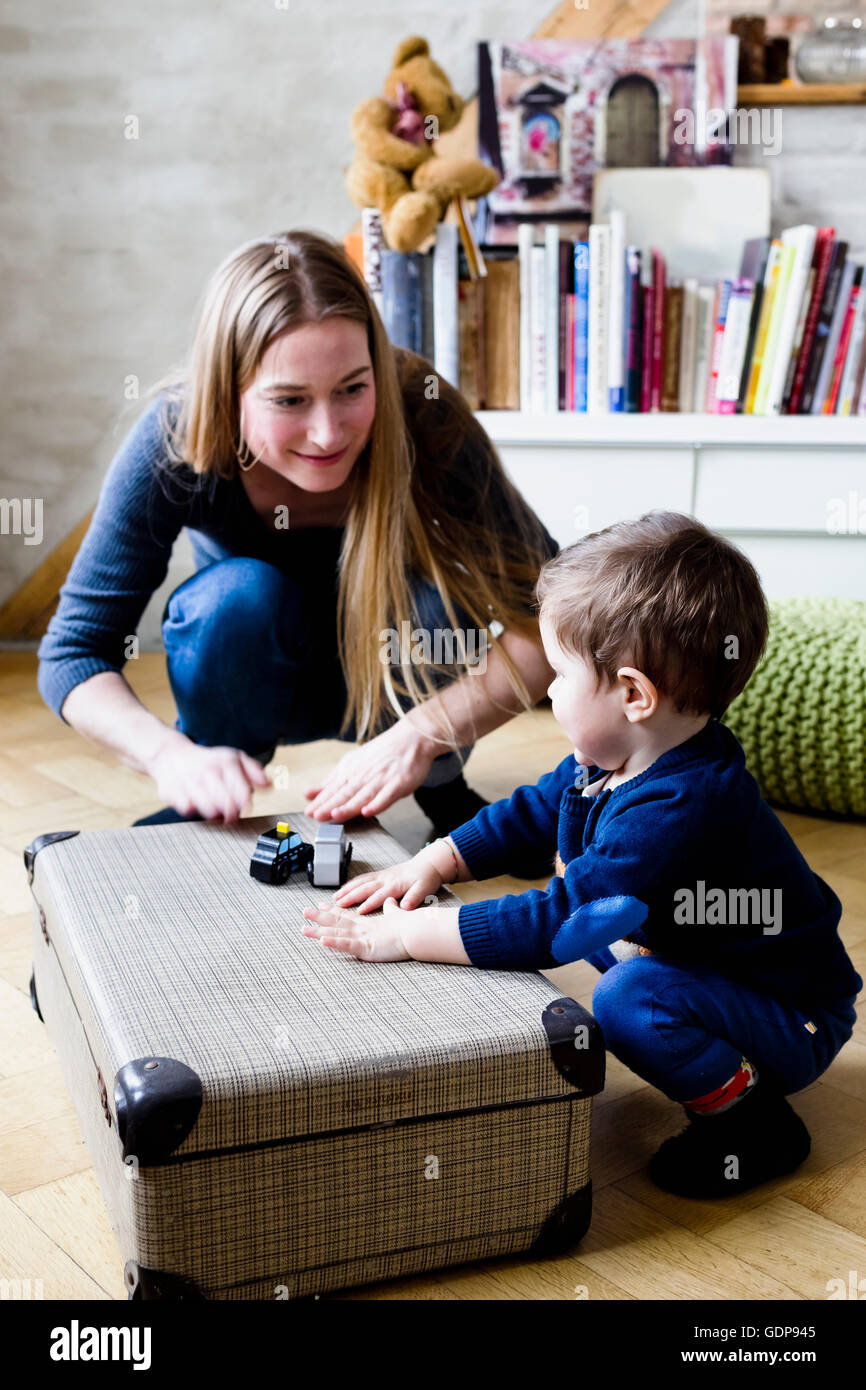 Mid adult woman drumming on suitcase with baby son on floor Stock Photo