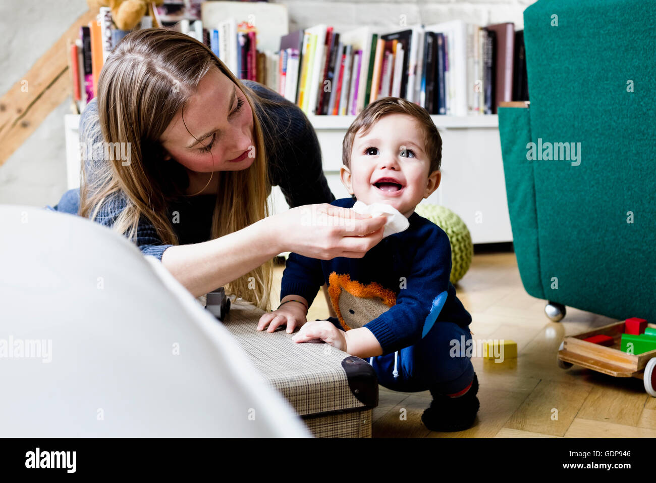 Mid adult woman wiping baby son's chin with tissue in living room Stock Photo