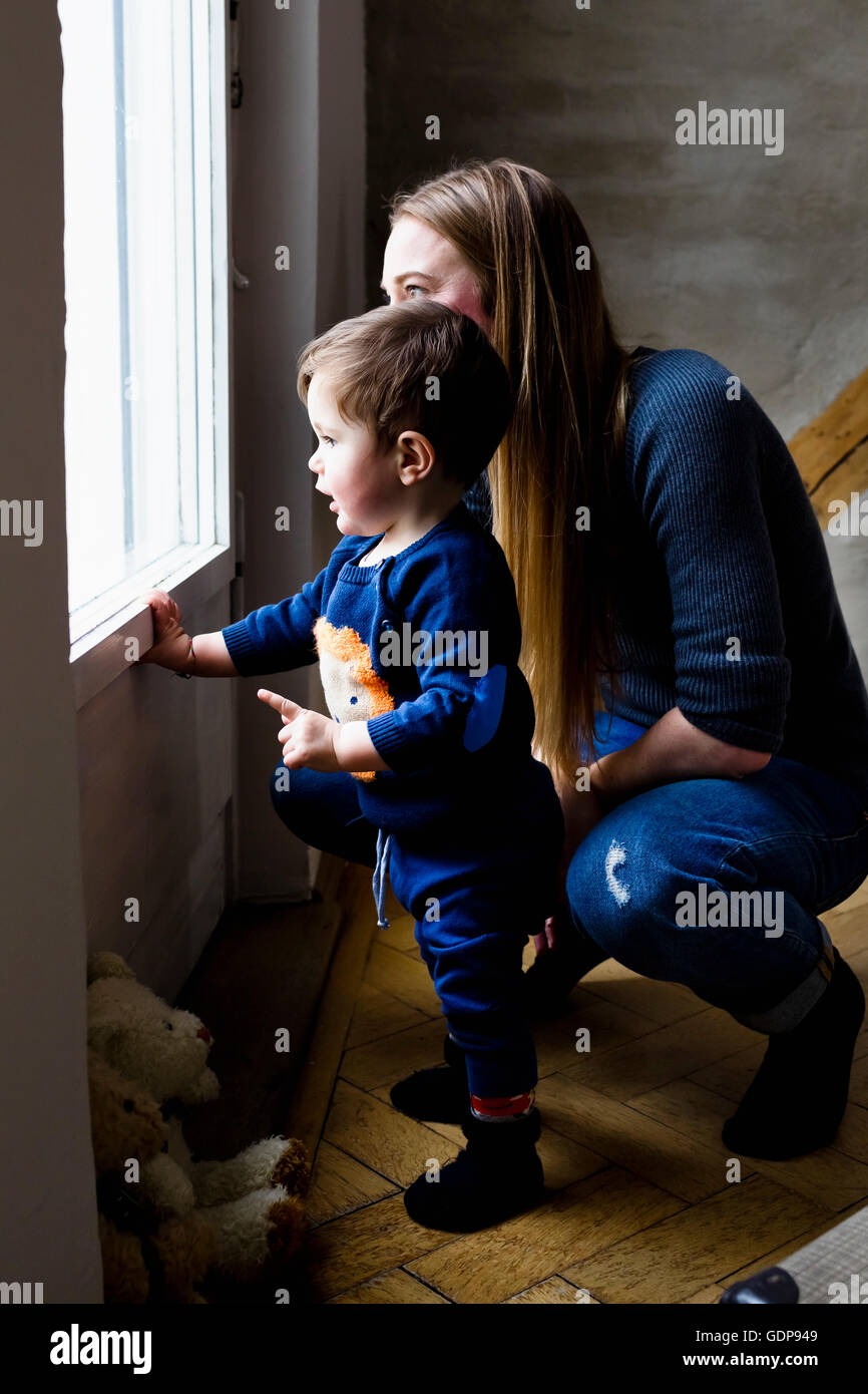Mid adult woman and baby son looking through living room window Stock Photo