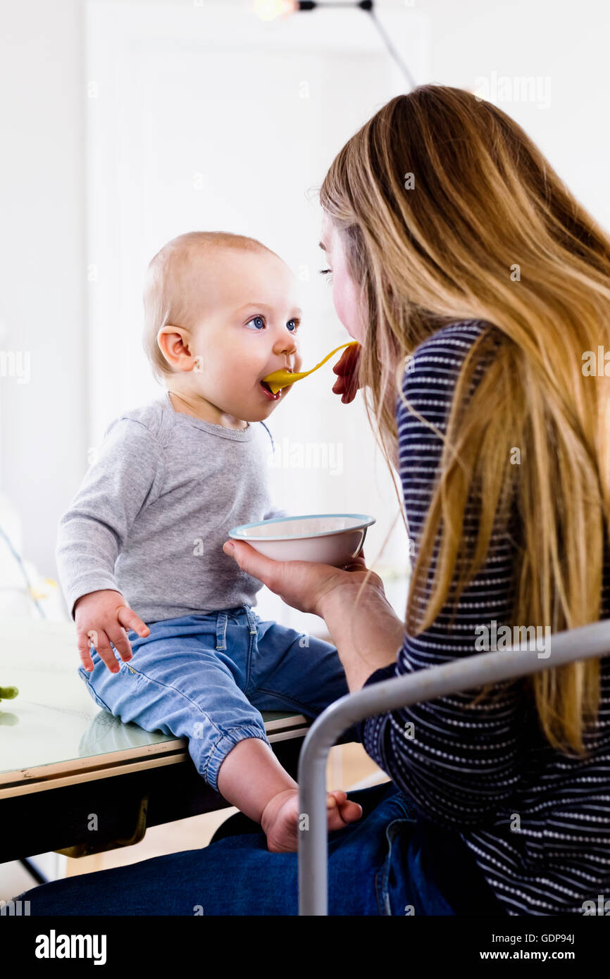 Mid adult woman feeding baby daughter on kitchen table Stock Photo