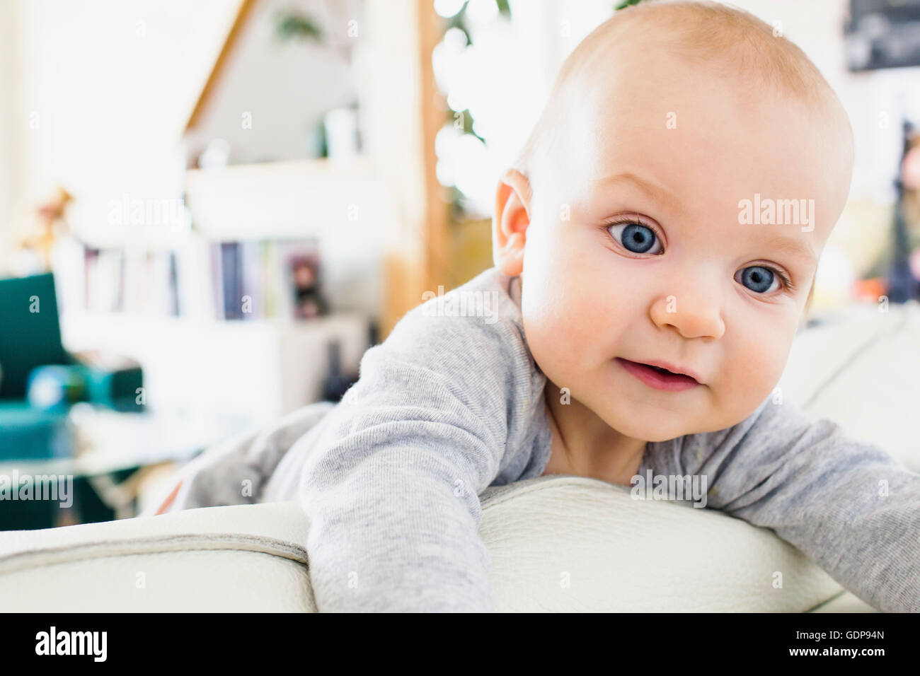 Blue eyed baby girl climbing on sofa Stock Photo