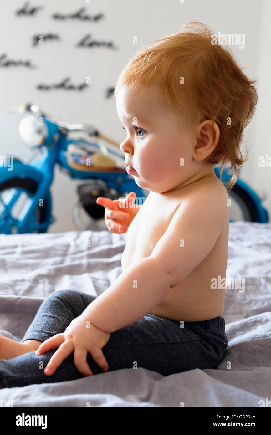 Baby girl sitting up on bed pointing finger Stock Photo