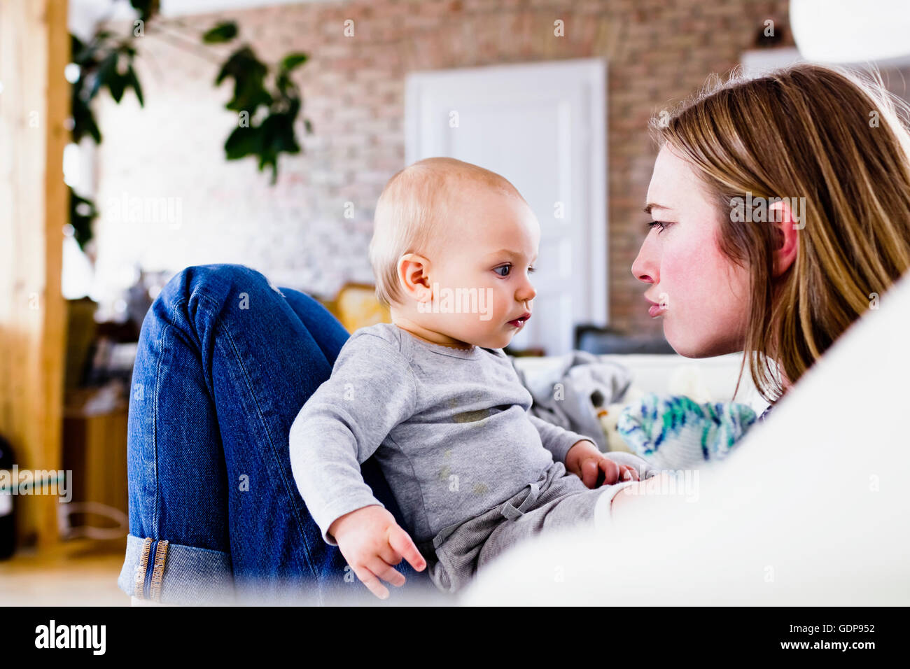 Mid adult woman and baby daughter pulling faces on sofa Stock Photo