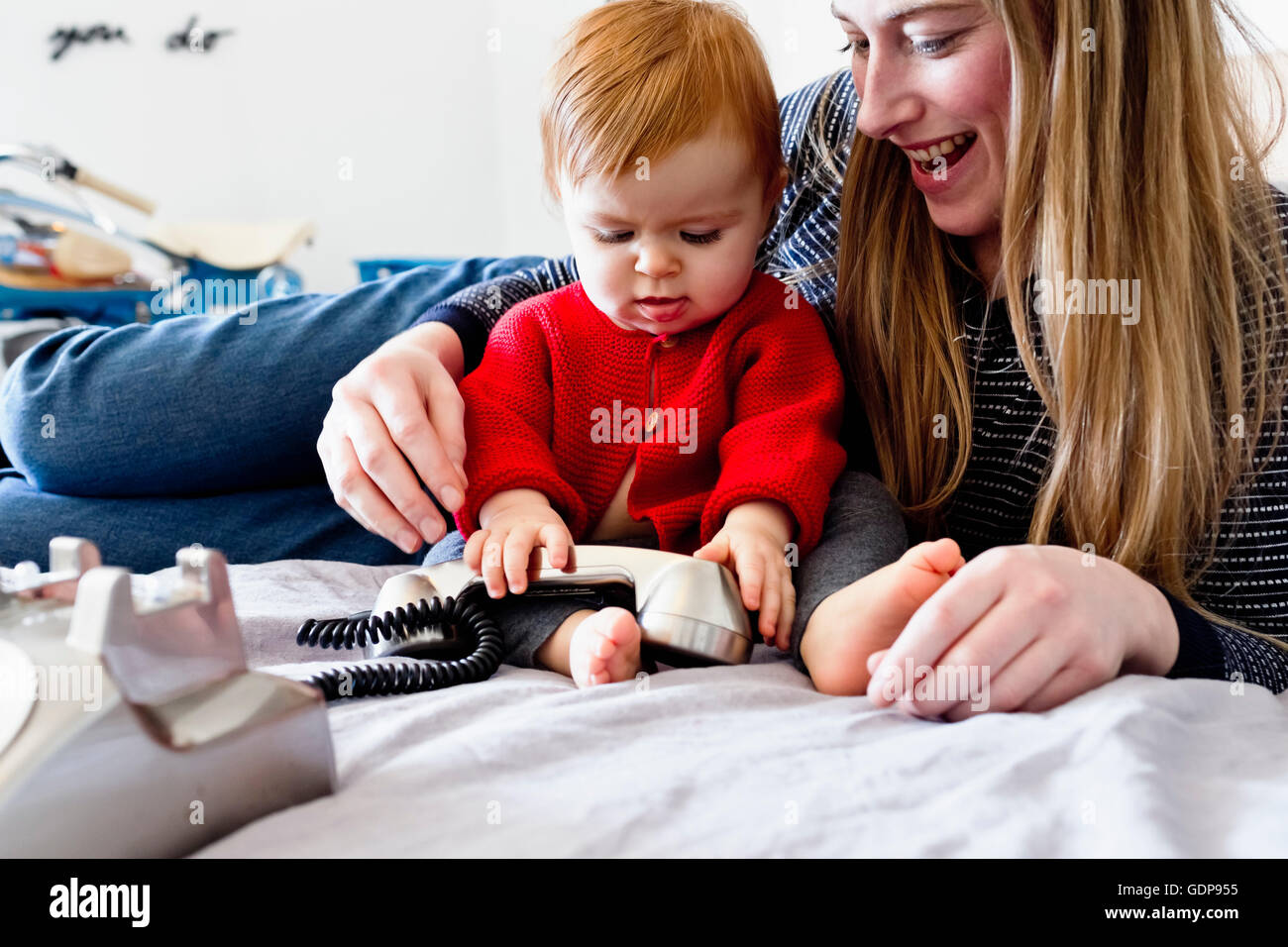 Baby girl and mother on bed playing with landline telephone Stock Photo