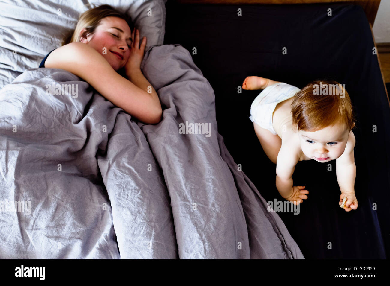Baby girl crawling on bed while mother relaxes Stock Photo