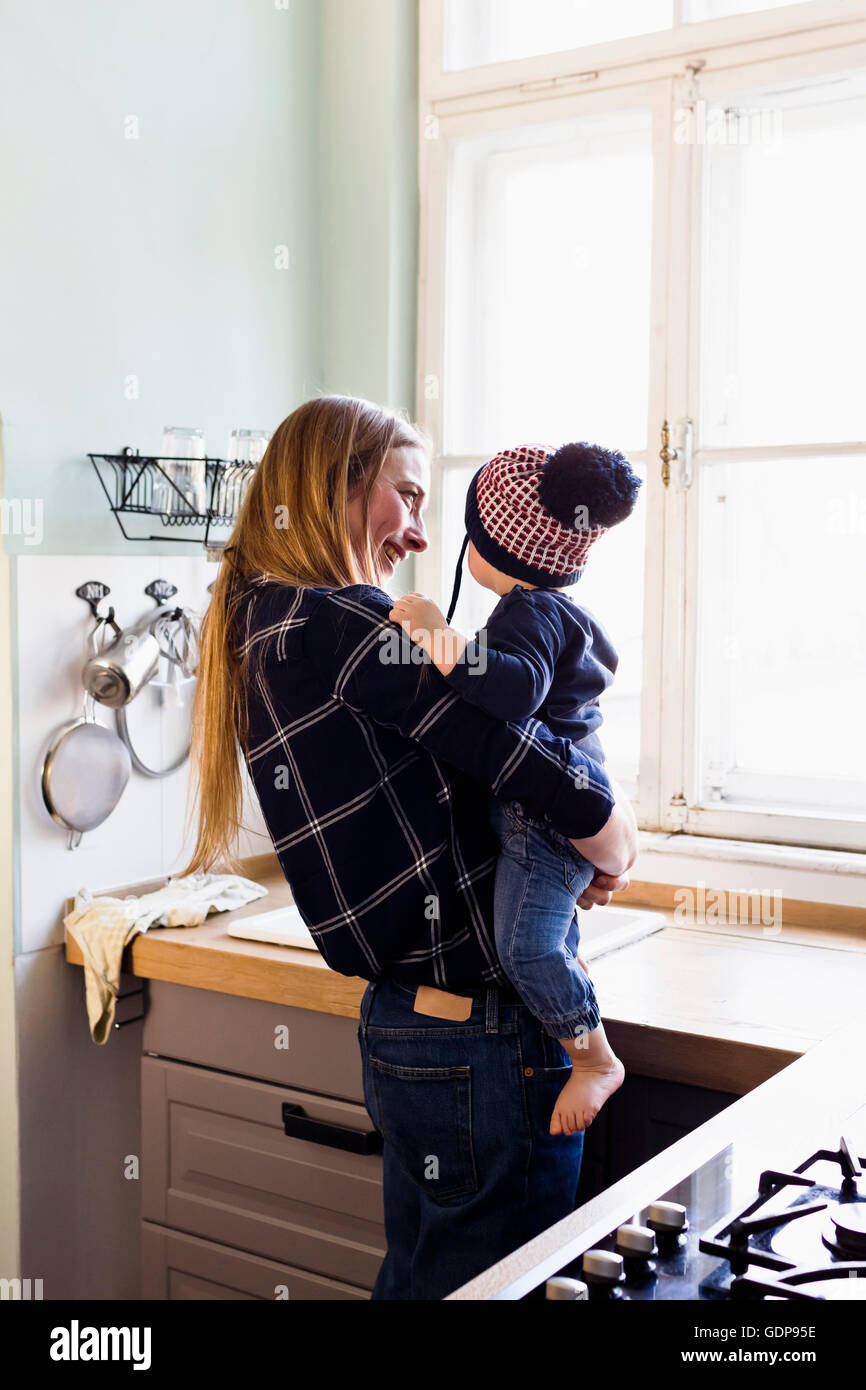 Mid adult woman carrying baby son in kitchen Stock Photo