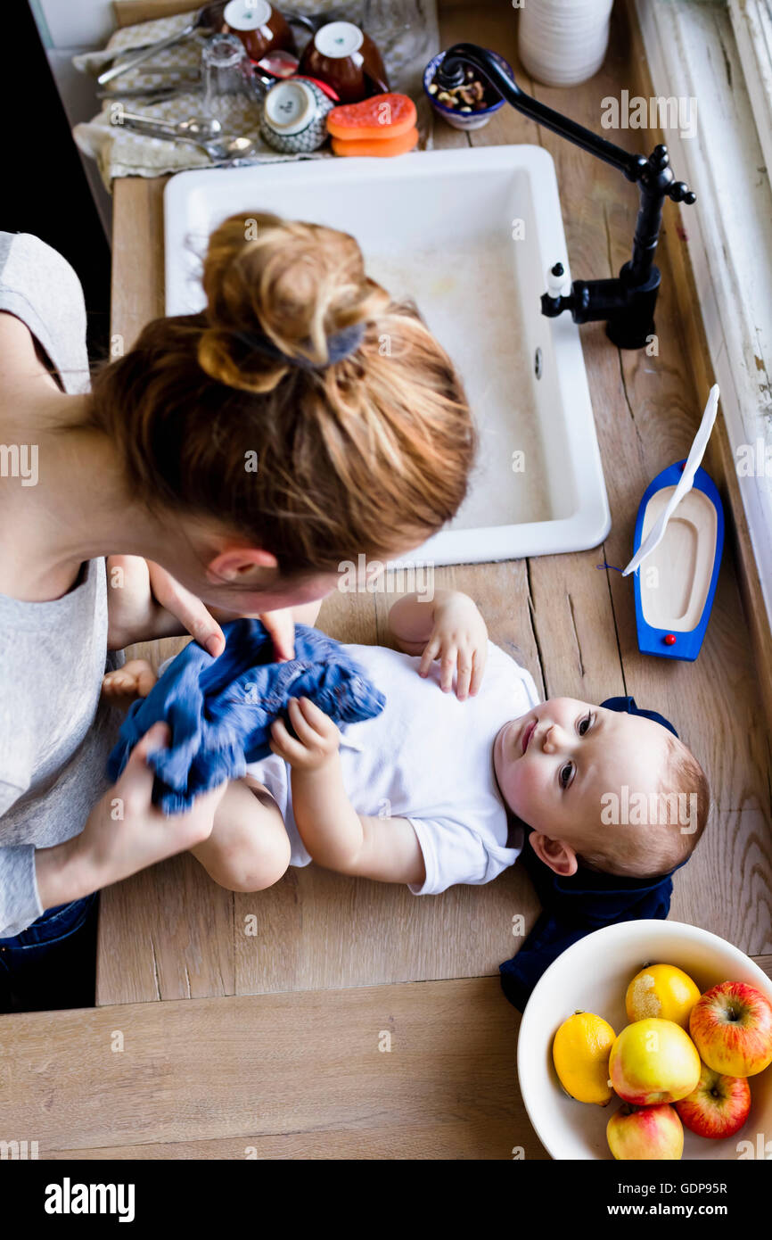 Overhead view of woman undressing baby son for bath in kitchen sink Stock Photo