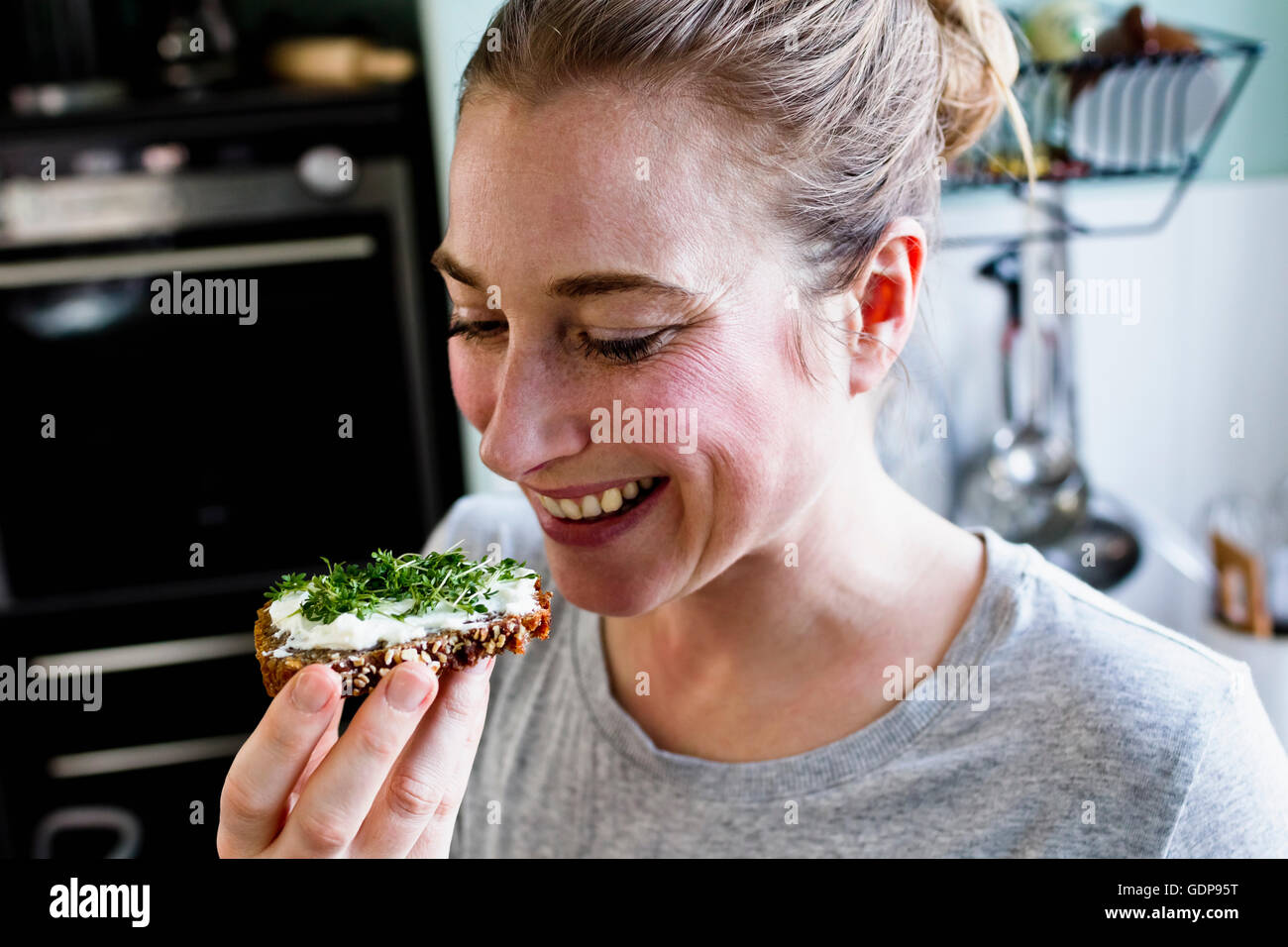 Mid adult woman eating rye bread snack in kitchen Stock Photo
