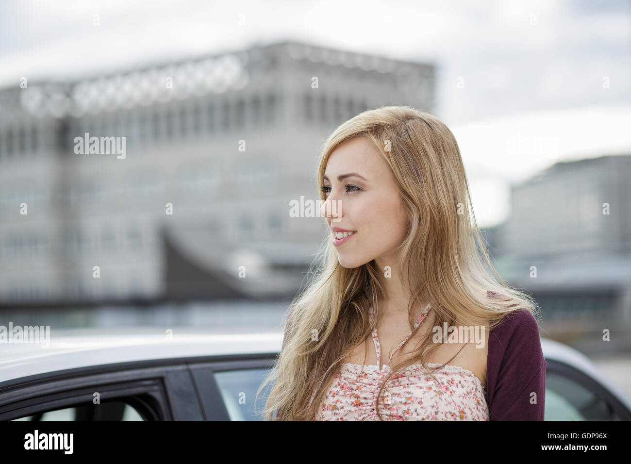 Long haired blond young woman waiting by car in city Stock Photo