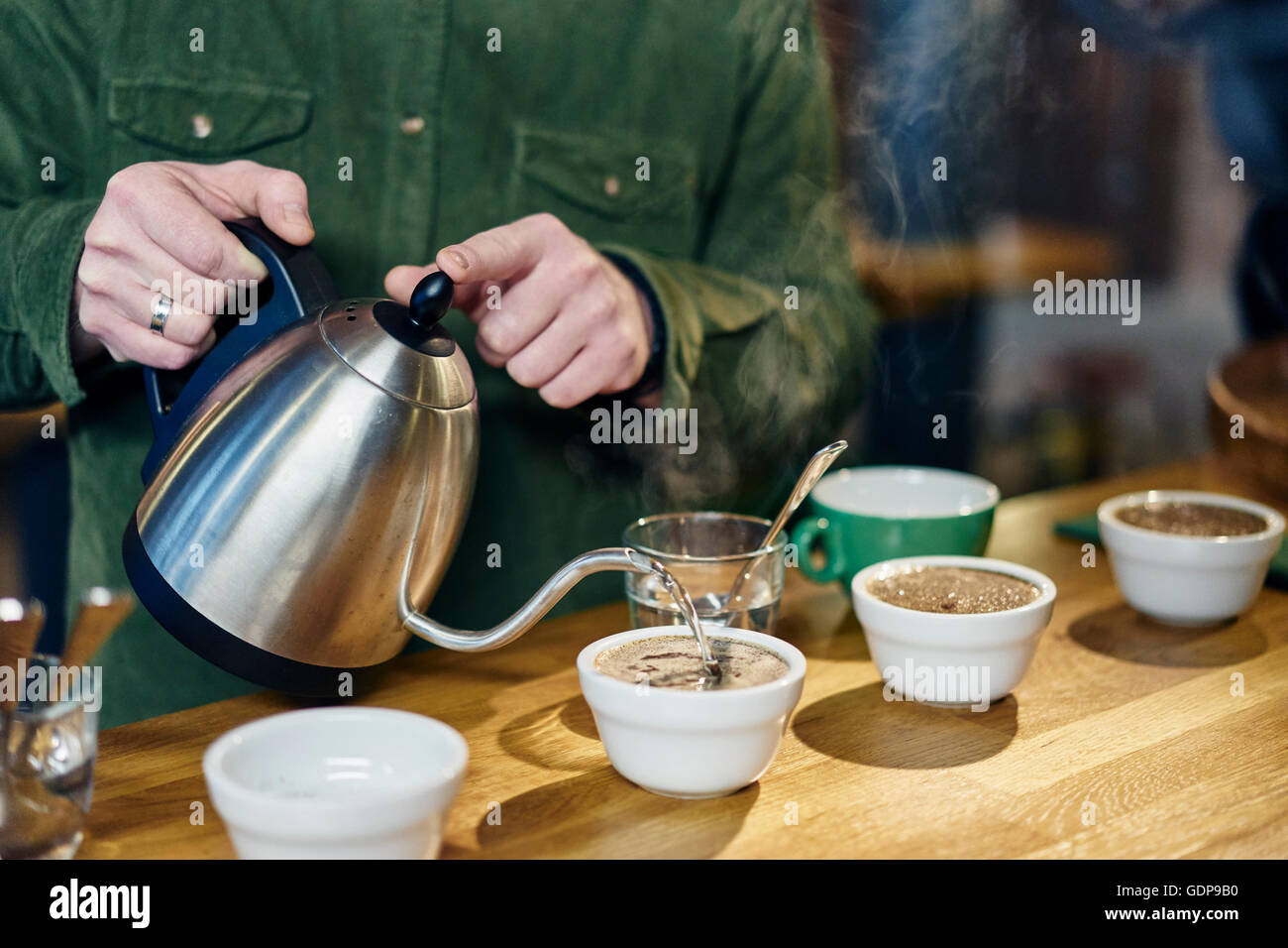 Man pouring boiling water into coffee bowls for tasting on coffee shop counter Stock Photo