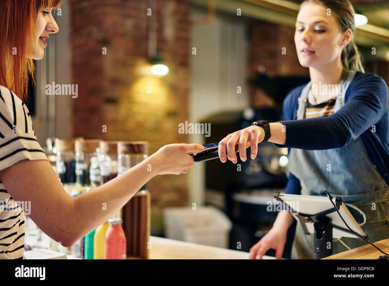 Female barista taking smartphone contactless payment from coffee shop customer Stock Photo